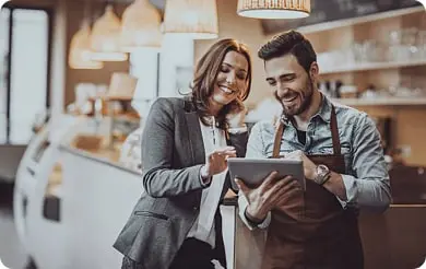 A smiling woman and man stand in a store looking at a tablet together.
