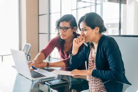 Two businesswomen talk while looking at a computer