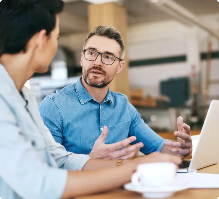 A man sitting with his laptop talks to his associate