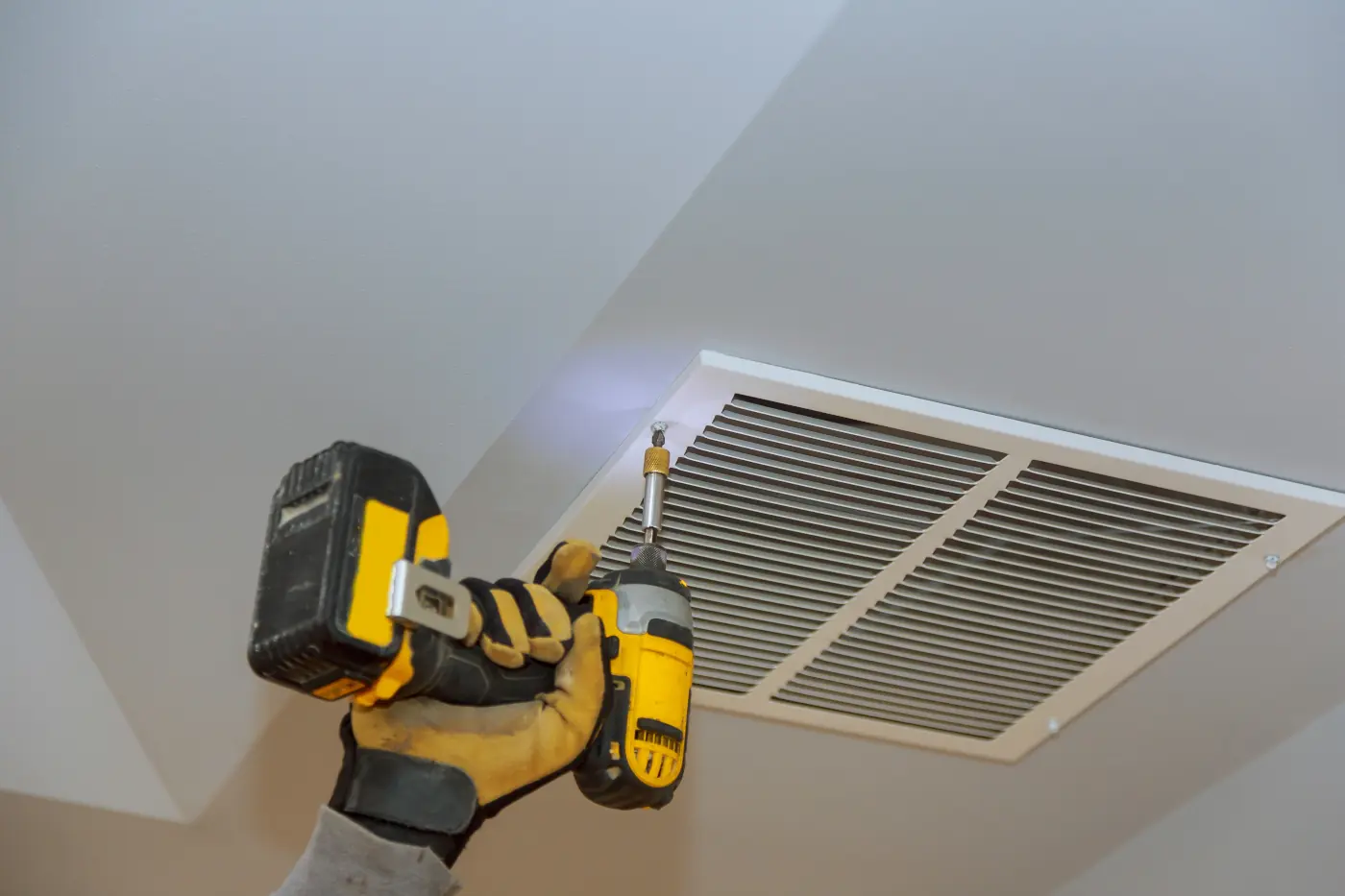 Technician with a cordless drill adjusting a ceiling vent.