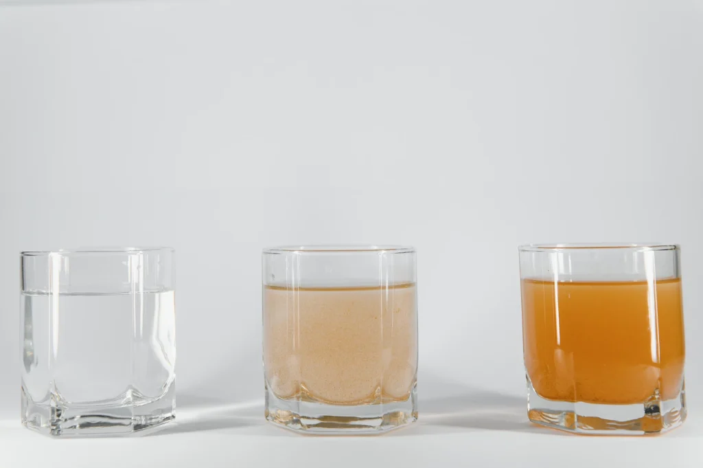 Three glasses of water showing varying levels of clarity and color on a plain white background.