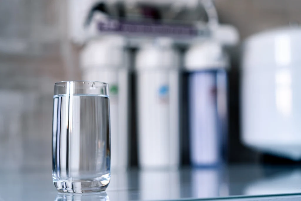 A glass of clear water on a reflective surface with water filters in the blurred background.