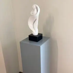 White sculpture on a grey lacquer rectangle pedestal with a black base