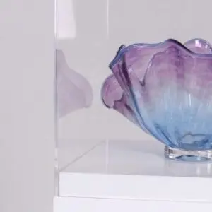 Purple and blue glass bowl on a white pedestal inside an acrylic display case