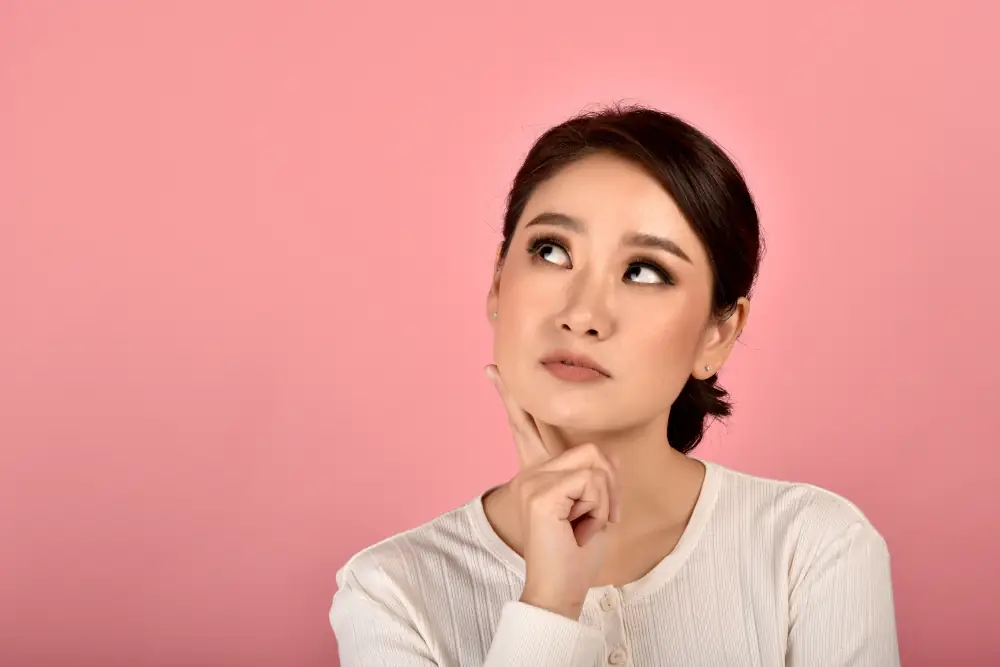 Heating Oil Versus Natural Gas From A London, ON Perspective - Asian woman thinking. Background is an isolated pink color.