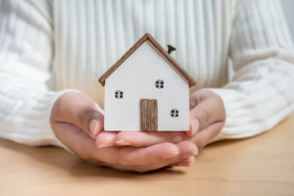 Hands holding small wooden house concept of a protection plan.
