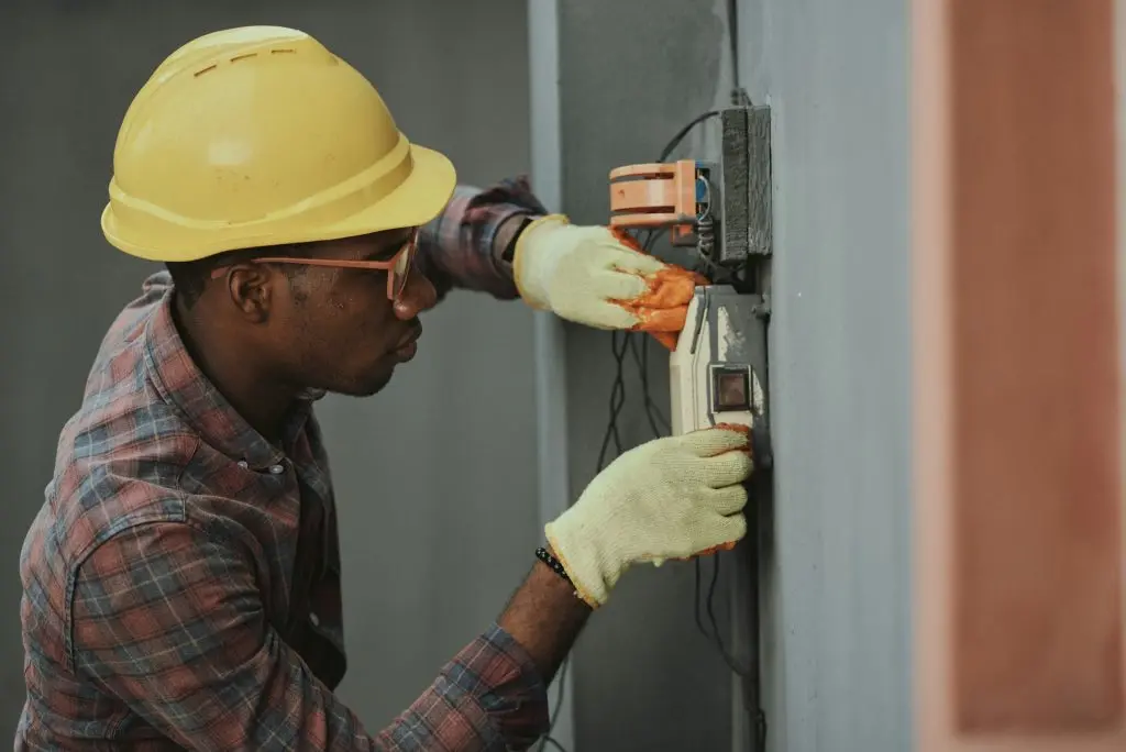 Electrician in a hard hat testing wiring with a meter