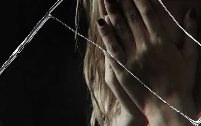 Close-up of a distressed woman holding her face in hands, viewed through cracked glass symbolizing trauma and legal reporting.