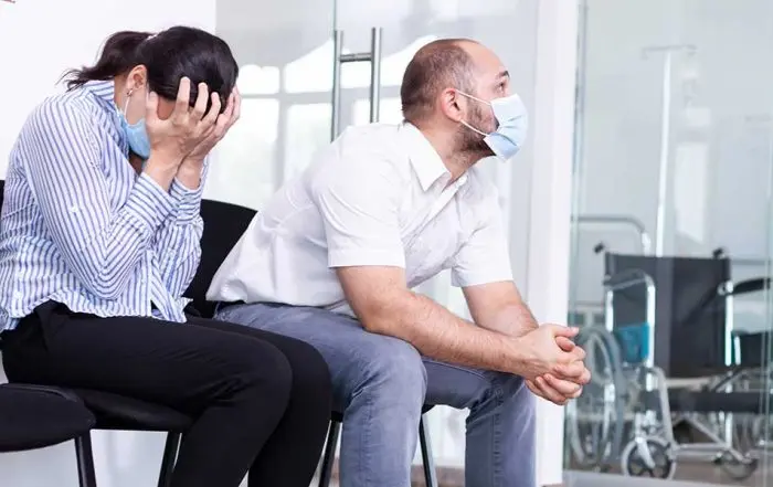 Distressed man and woman wearing face masks sitting in a hospital waiting room following a personal injury accident incident.