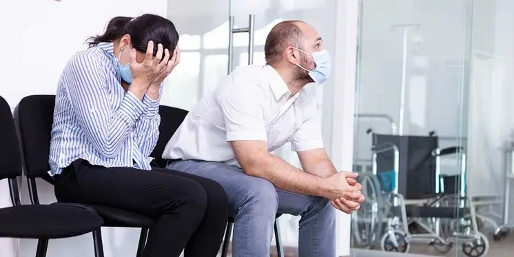 Distressed man and woman wearing face masks sitting in a hospital waiting room following a personal injury accident incident.
