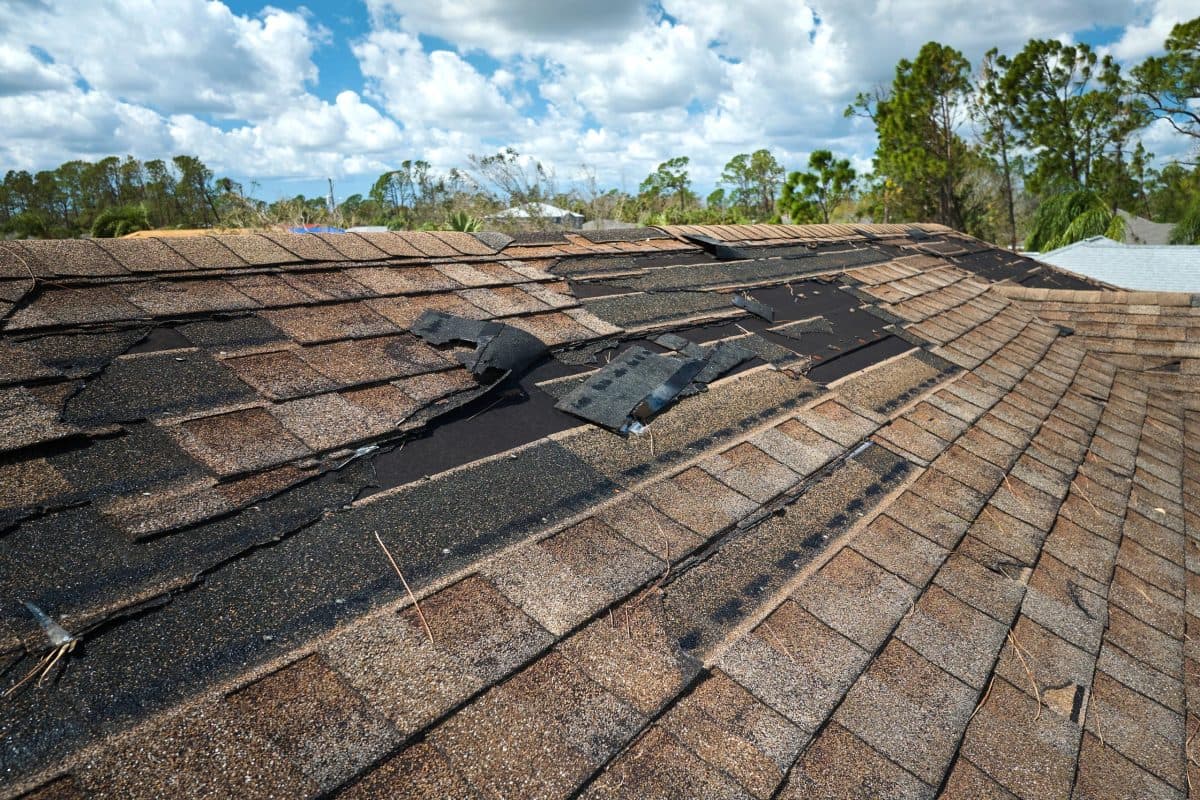 storm damage roof replacement Damaged house roof with missing shingles after hurricane Ian in Florida. Consequences of natural disaster.