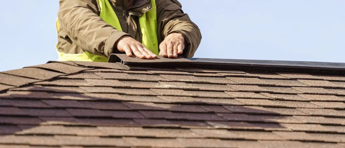 How to install ridge cap shingles: Workman installing shingle roof on new home under construction
