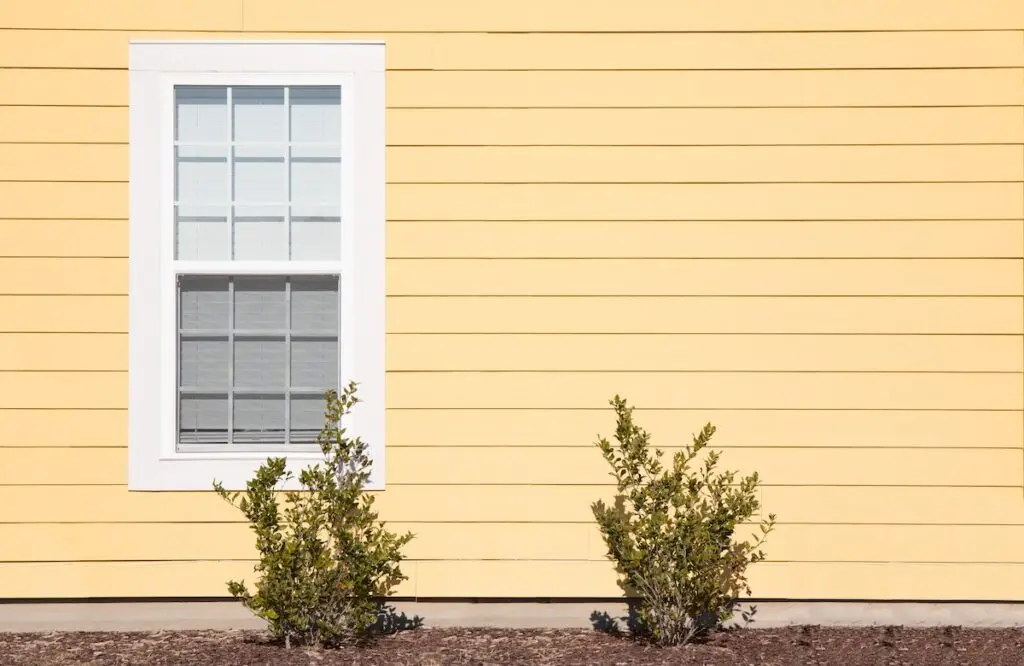 An exterior shot of a single window with bright yellow siding.
