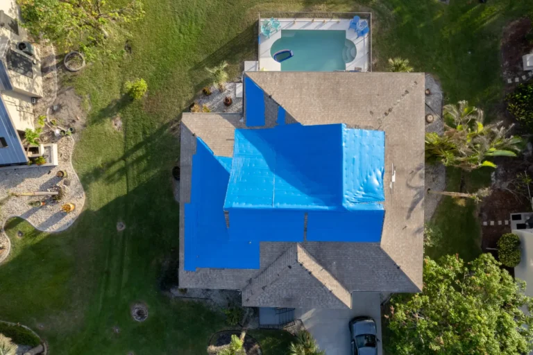 Aerial view of a home with blue tarps covering storm-damaged asphalt shingle roof sections