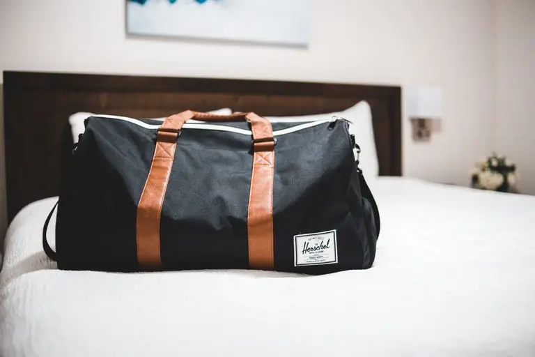 Contemporary baggage bag with inscription on white bed cover in light hotel room