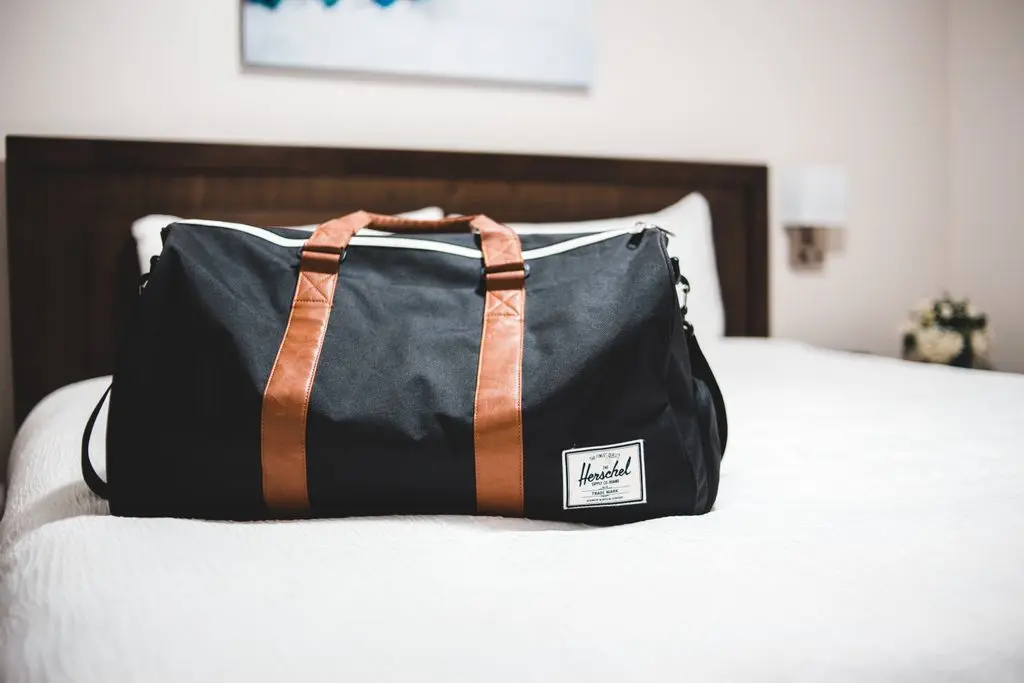 Contemporary baggage bag with inscription on white bed cover in light hotel room