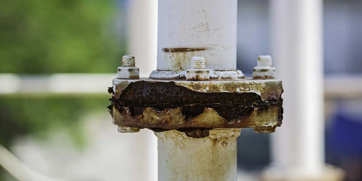 A white outdoor metal pipe joint displaying severe rust damage and corrosion caused by exposure to salty coastal air.