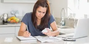 Frustrated woman holding a paper statement at her kitchen counter, confused by a high water bill from hidden leaks.