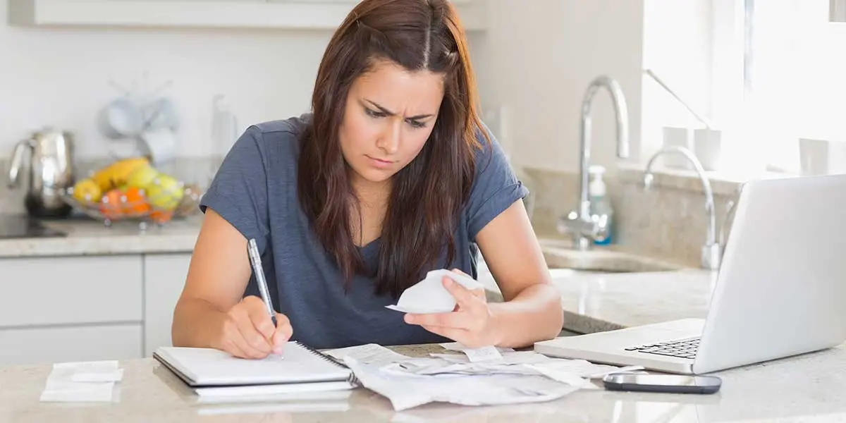 Frustrated woman holding a paper statement at her kitchen counter, confused by a high water bill from hidden leaks.