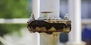 A white outdoor metal pipe joint displaying severe rust damage and corrosion caused by exposure to salty coastal air.
