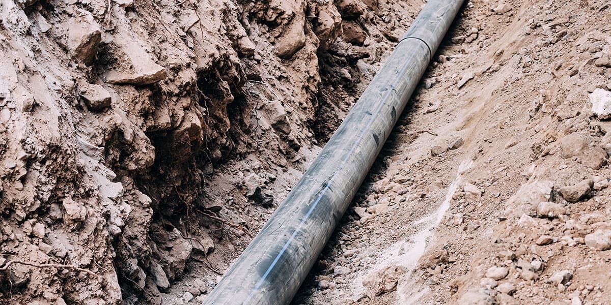 Long black underground sewer pipe laid inside a deep dirt trench during plumbing excavation to prevent sagging or pipe failure.