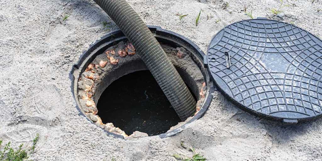 A large vacuum hose is inserted into an open sewer cleanout manhole during main sewer line maintenance.