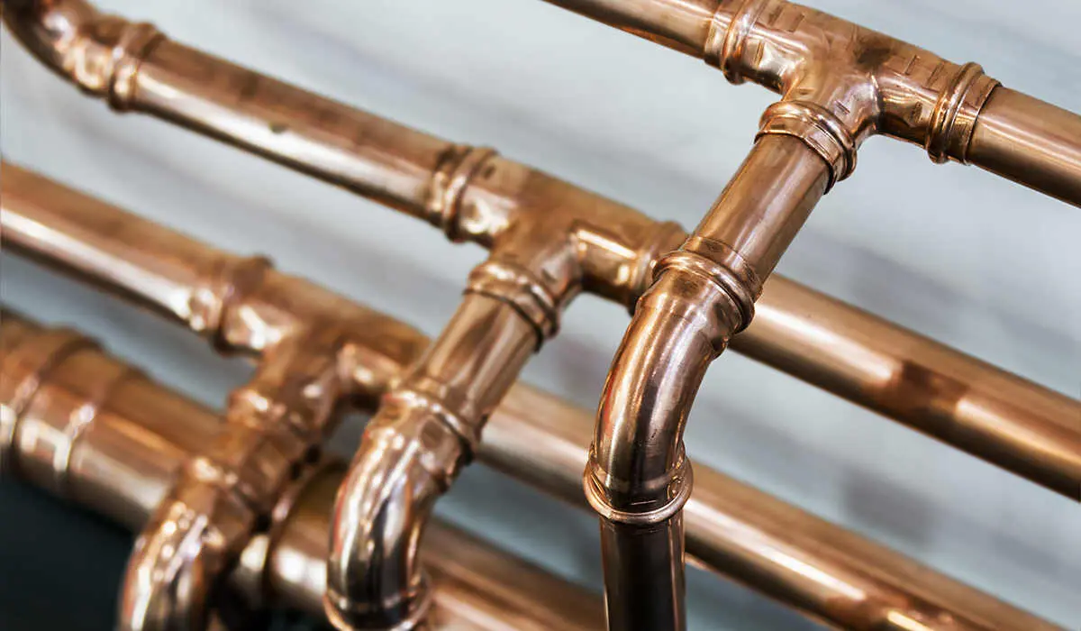 A network of polished copper plumbing pipes with press-fit fittings running alongside a wall in a building.