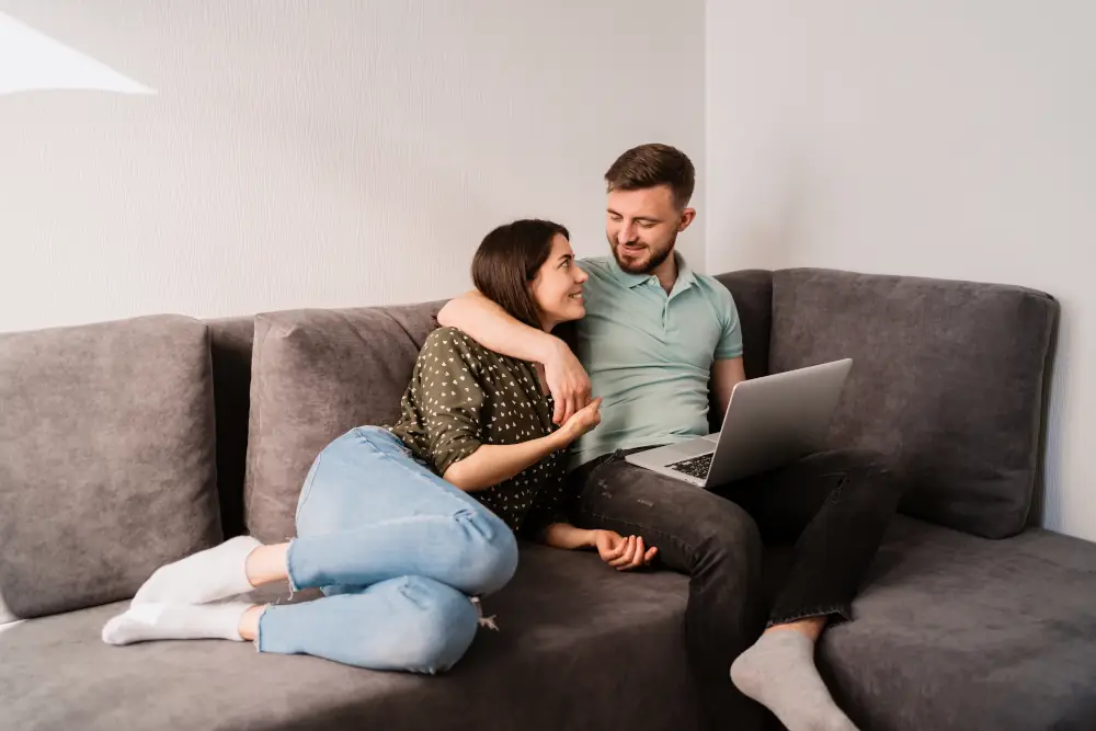 The Benefits of Investing in Energy-Efficient HVAC Systems - Couple sitting on sofa. Both are looking down at a laptop