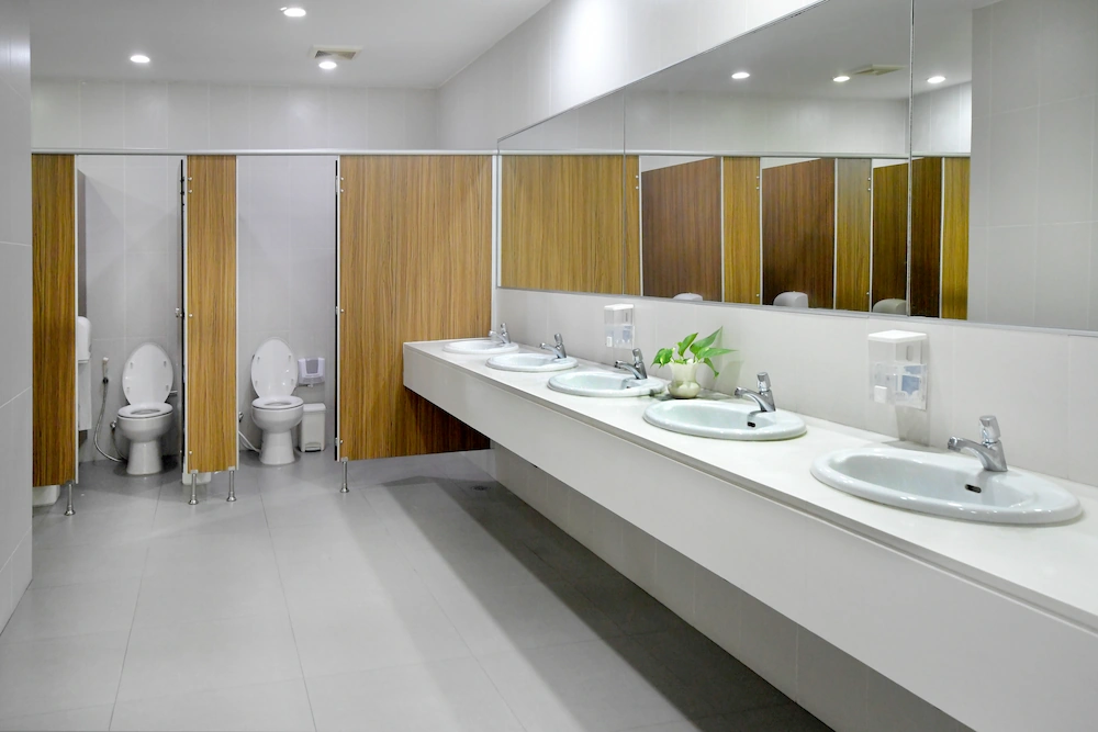 Empty public bathroom with white sinks and wide wall mirror, and toilets