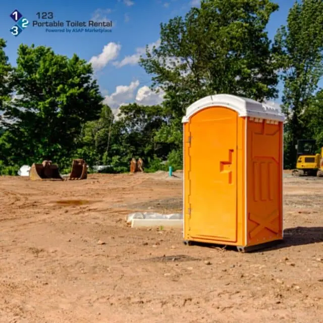 Bright orange portable toilet on a construction site – 123 Portable Toilet Rental unit positioned for worker access with heavy equipment in background.