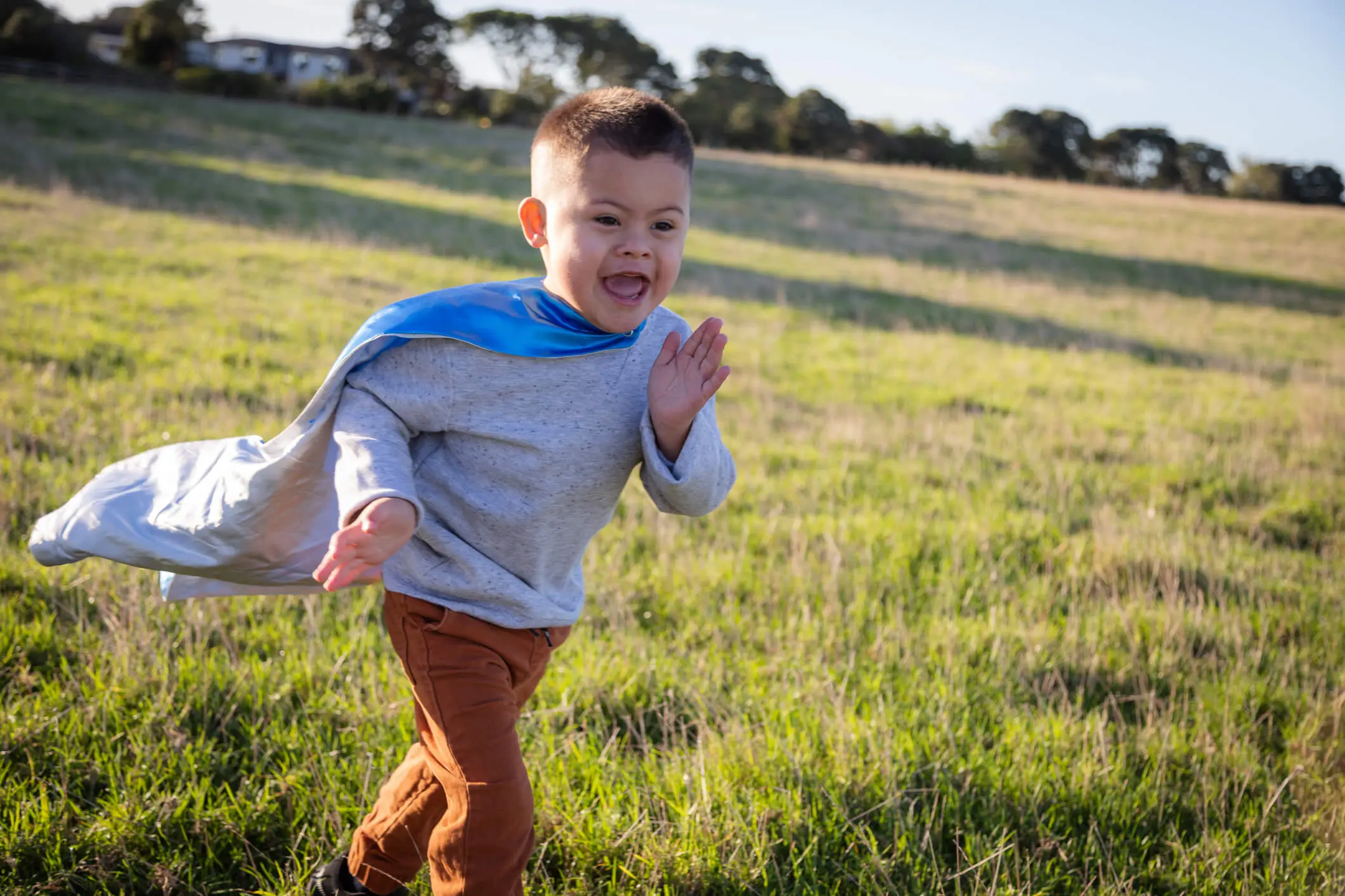 Little boy excitedly running through field wearing cape