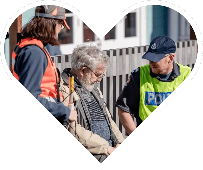 Elderly man sitting on a bench with police and woman in high vis vest