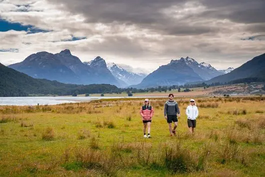 Three guests walking across a paddock near Diamond Lake, with mountains behind