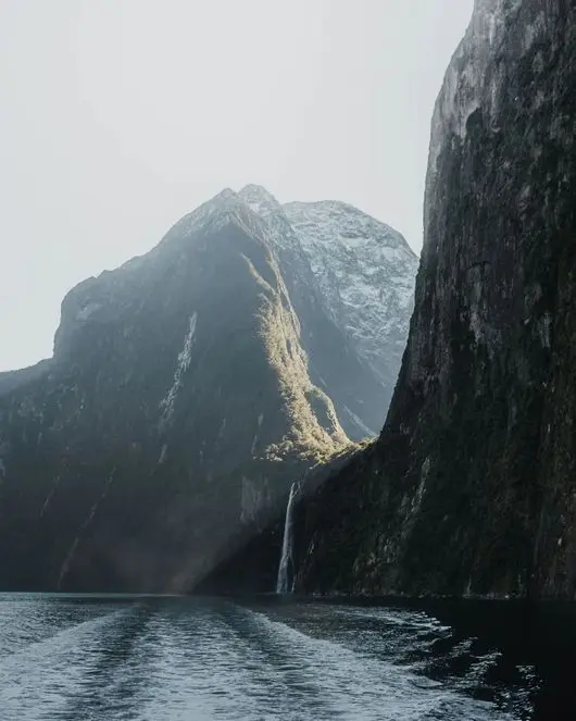 Waterfall falling down a sheer cliff into Milford Sound, seen from the water