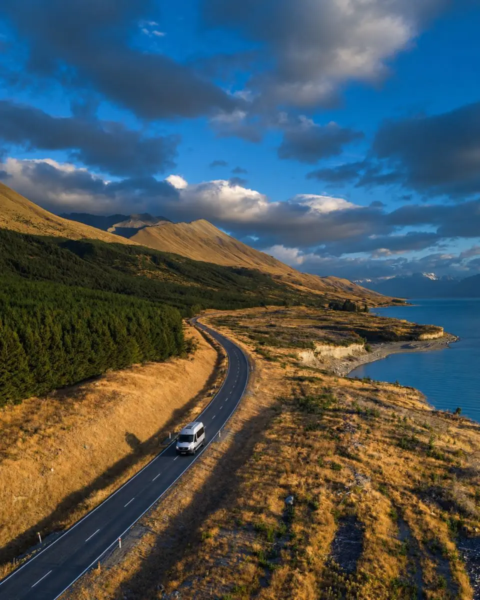 Tour van driving a lakeside road through golden hills