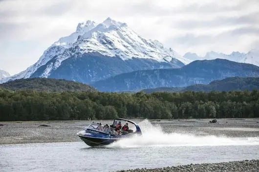 Dart River Jet Safari boat speeding along the river below snow-capped mountains