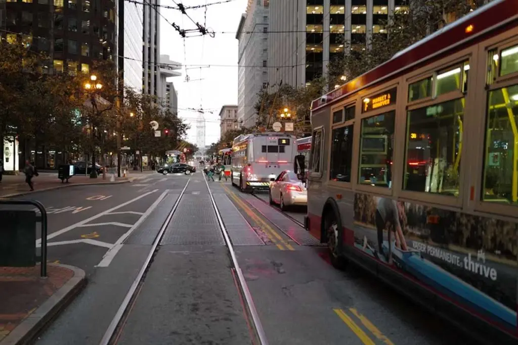 Transit bus with a Kaiser Permanente ad traveling an urban corridor with trolley wires overhead at dusk.