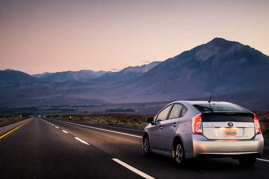 Toyota Prius driving along an open highway shoulder toward a mountainous horizon at twilight.