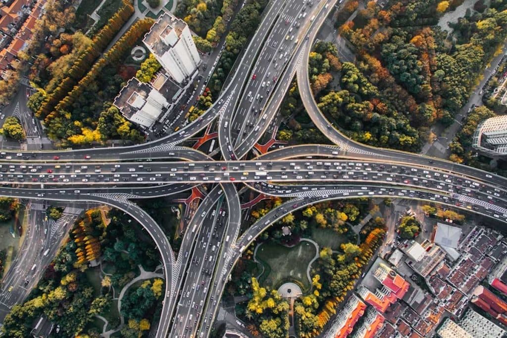 Aerial view of a multi-level highway interchange weaving over dense urban parkland and footpaths.