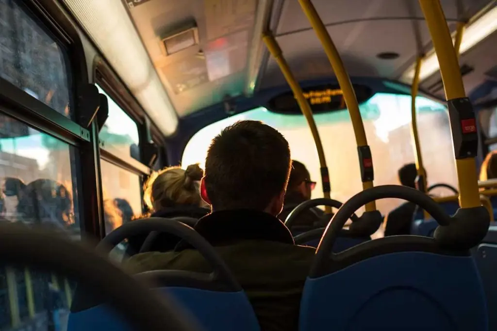 Passengers seated inside a transit bus as golden-hour light streams through the windshield.