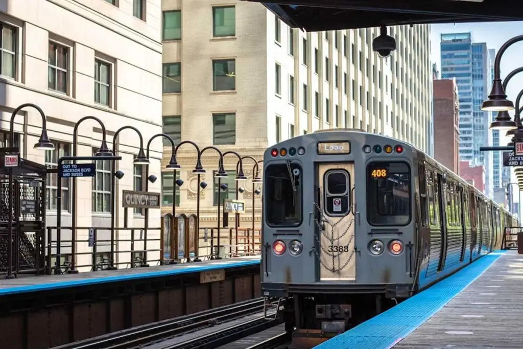 Elevated transit train pulling into a historic open-air station platform with vintage lampposts.