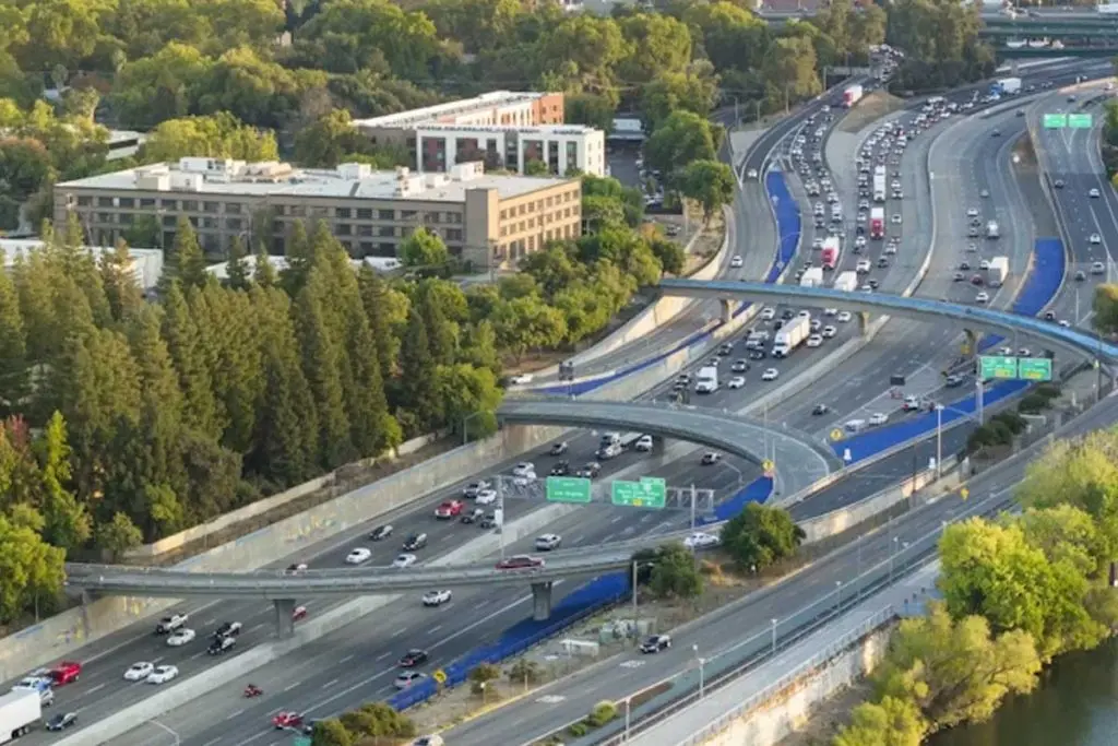 Aerial view of a multi-lane highway interchange with heavy traffic flowing past office complexes and greenery.