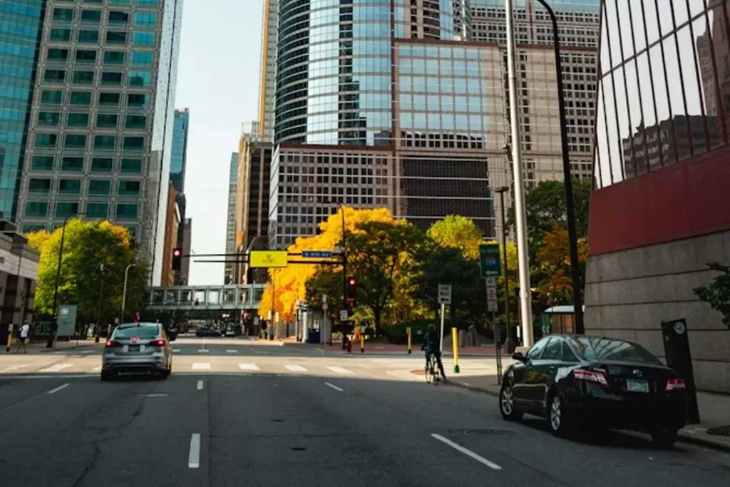 Cyclist riding near a downtown intersection past autumn trees and modern glass skyscrapers.