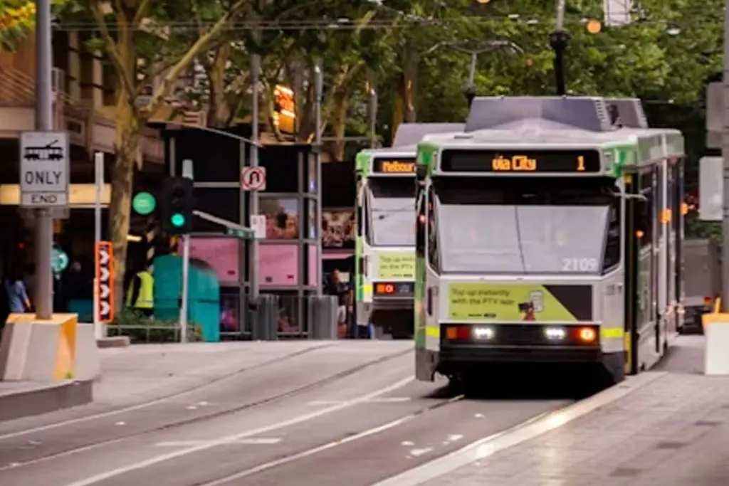 Modern city tram traveling along central street tracks past a boarding platform.