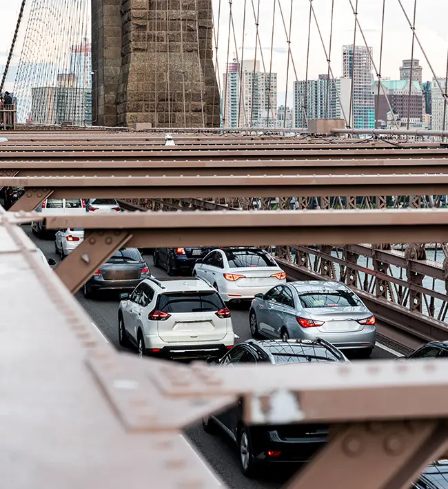 Vehicles queued in traffic on a bridge roadway framed by steel truss beams.
