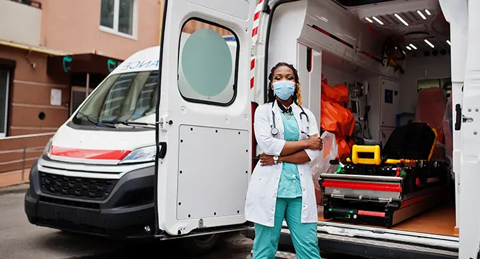 Female paramedic standing in front of an open ambulance equipped with a stretcher and emergency medical gear.