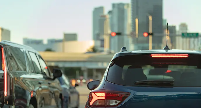 Vehicles stopped at red traffic lights beneath an elevated highway, with a modern city skyline in the background.