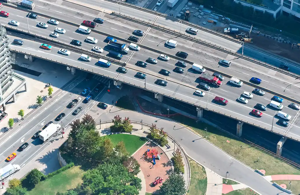 Aerial photograph showing heavy traffic on an elevated freeway overpass, with a park and children's playground visible below.