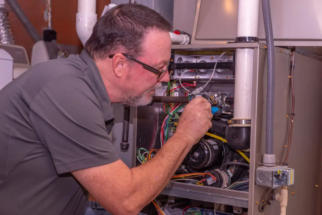 HVAC Tech Making Adjustments To Furnace Gray Shirt