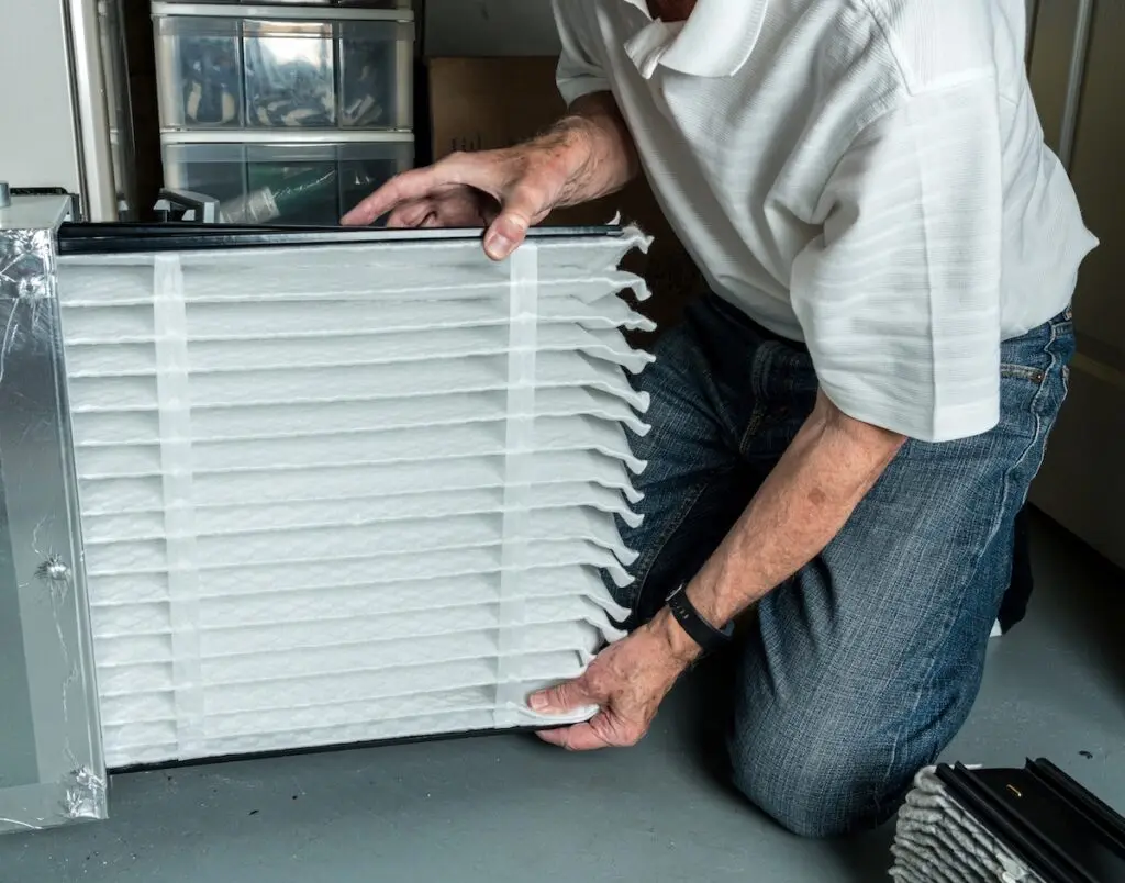 how to maintain heating and air conditioning Senior caucasian man checking a clean folded air filter in the HVAC furnace system in basement of home